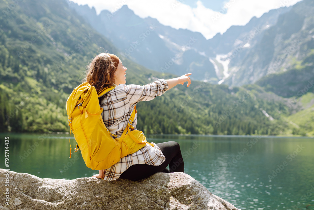 Happy tourist woman  enjoys the view of the mountain lake in sunny weather. Scenery of the majestic mountains. Active lifestyle.