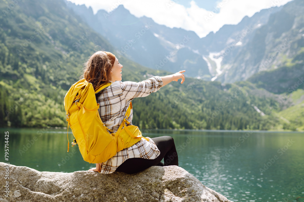Naklejka premium Happy tourist woman enjoys the view of the mountain lake in sunny weather. Scenery of the majestic mountains. Active lifestyle.