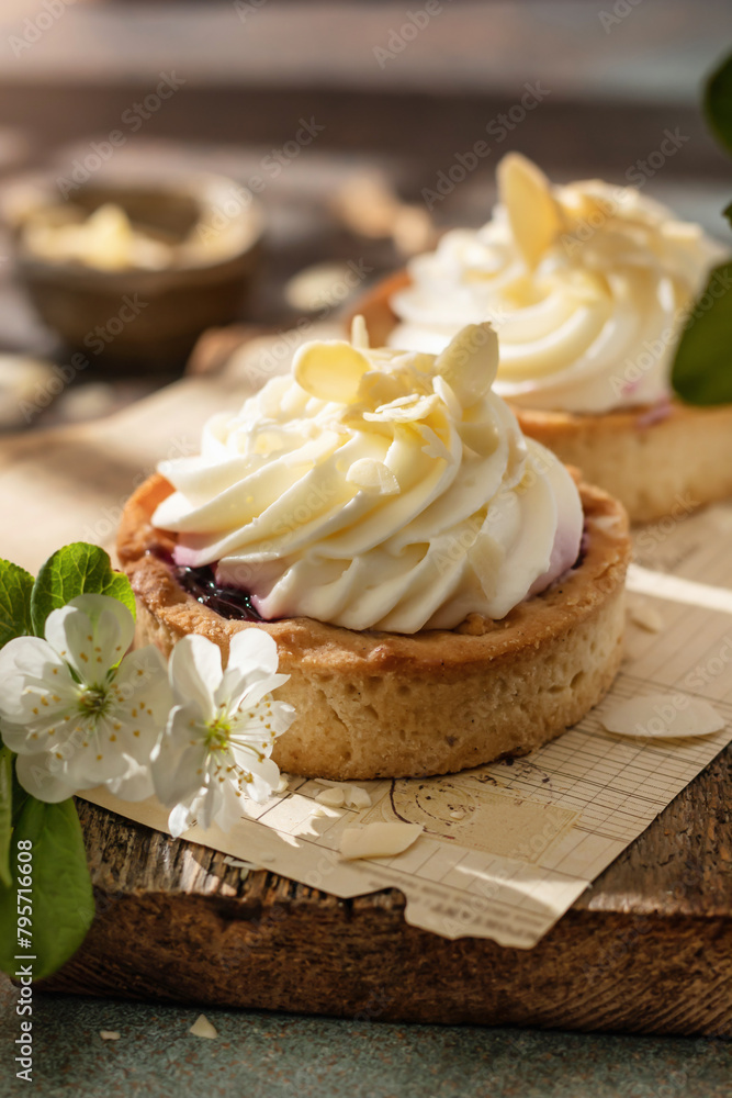 Sweet cream tarts on rustic wooden board in spring white flowers