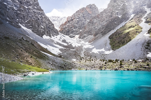 Mountain panorama, landscape with rocky peaks and blue turquoise lake Ziyorat in the Fan Mountains in Tajikistan, on a sunny summer day