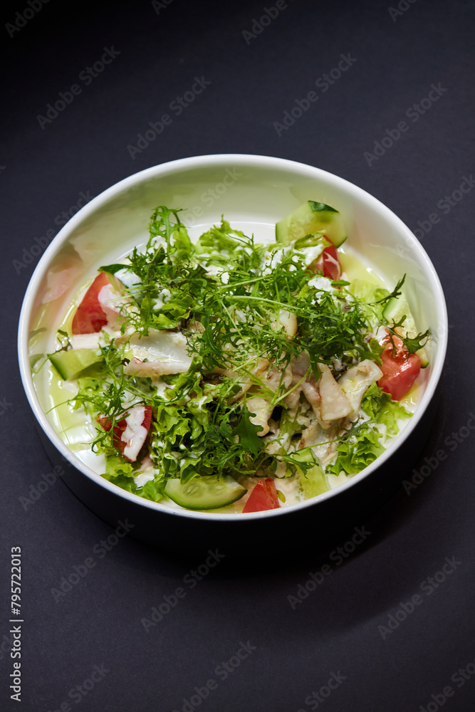 Salad dish with lettuce, tomatoes, and cucumbers on a black plate