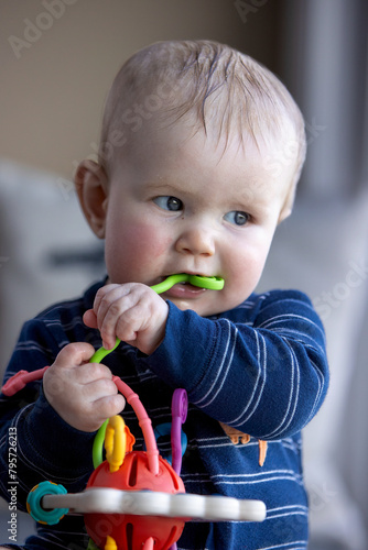 Six month old child sitting and chewing a toy.