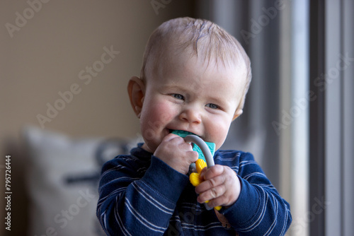 Smiling six month old child with a toy in his mouth.