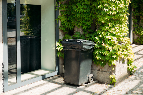 A black trash can sitting next to a wall. Ecology concept. Help to reduce waste, Help global warming. Garbage bin