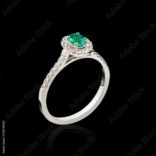 Beautiful white gold ring with diamonds and emerald on a black background