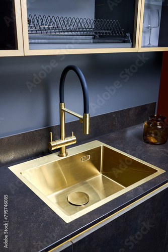 Luxurious interior square golden brass sink and faucet double tap mixer in contemporary modern design with stone marble stoneware countertop black and gold kitchen with sandwatch and glass pot photo