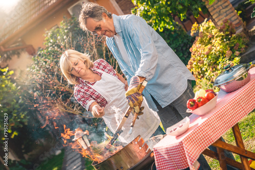 Lovely senior couple preparing barbecue together in backyard. Woman assisting to her husband while lighting a fire outdoors.