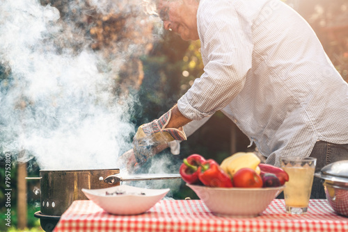 Close up of a male preparing barbecue in backyard. Senior man being busy with roasting meat and vegetable for Sunday lunch outdoors.