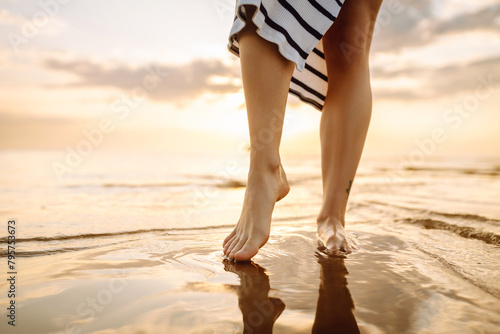 Slim female legs and feet walking along sea water waves on sandy beach. Pretty woman walks at seaside surf. The concept of relax, travel, freedom and summer vacation.