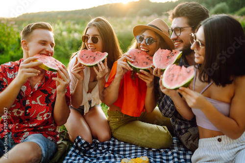 Group of friends having fun eating watermelon on the picnic outdoors. Foods, travel, nature and vacations concept