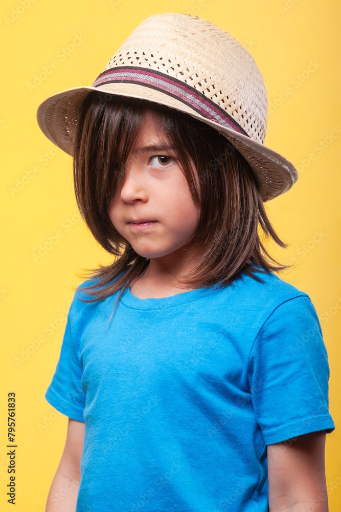 Portrait of boy with blue t-shirt, straw hat and long brown hair looking at camera. Portrait of boy with blue t-shirt, straw hat and long brown hair looking at camera.