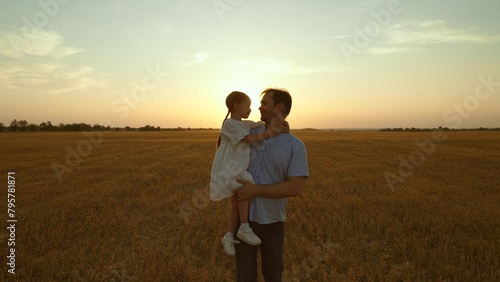 Father holding kid in arms in field at sunset. Happy cheery parent child kid strolling moving going across huge yellow meadow. Girl sits in man arms pointing with finger. Love fatherhood parenthood