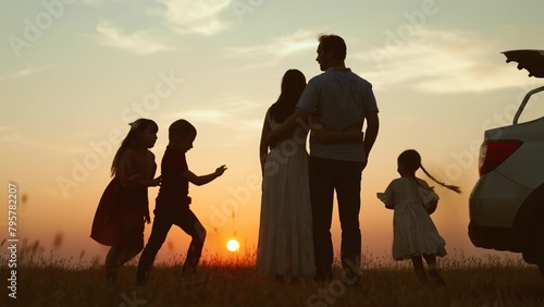 Family at sunset near car silhouettes. Kids children with ball running around parents enjoying picnic in nature park. Bringing family closer strengthening relationships outdoor outside activities.