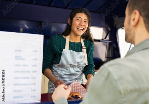 A friendly food truck worker shares a laugh with a customer during a sunny day's service photo