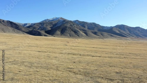 A vast, empty desert with a mountain range in the background. The sky is clear and blue, and the sun is shining brightly. The scene is peaceful and serene