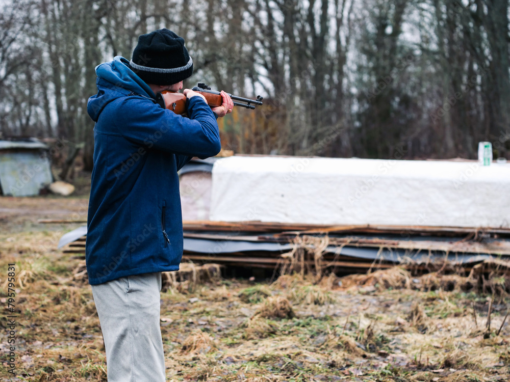Man holding small caliber rifle for shooting practice in a country side. Sport and entertainment. Male with grey beard in blue jacket and dark hat. Out door activity. Man holding small caliber rifle for shooting practice in a country side. Sport and entertainment. Male with grey beard in blue jacket and dark hat. Out door activity.
