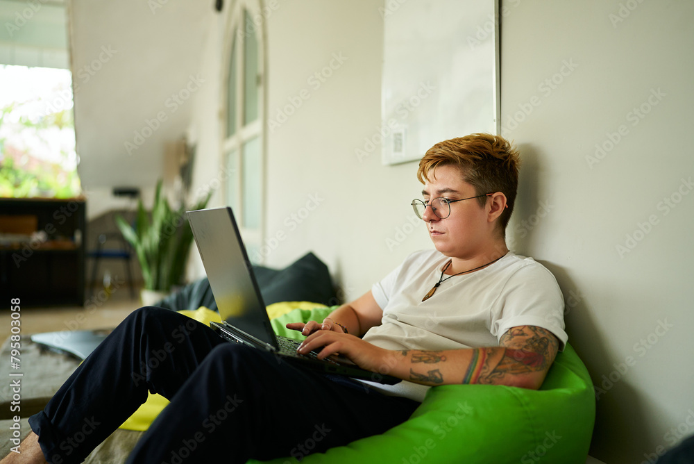 custom made wallpaper toronto digitalTransgender pro works on laptop from cozy bean bag in modern coworking space. Focused on screen, person enjoys flexible working environment. Inclusive workplace, remote job and casual office setup.