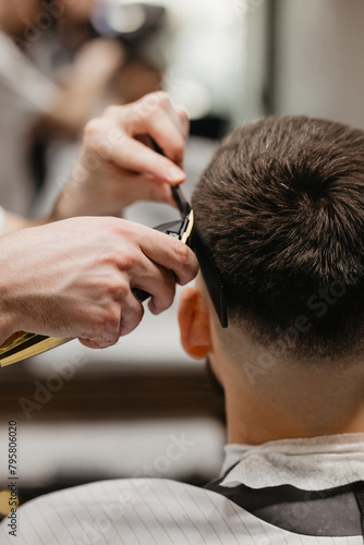 Barber uses clipper on mans hair, near forehead, ear, chin, temple