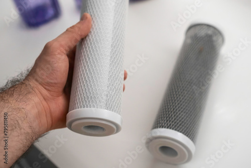 Man holding new carbon filter for reverse osmosis purification water system, while dirty lies on the table