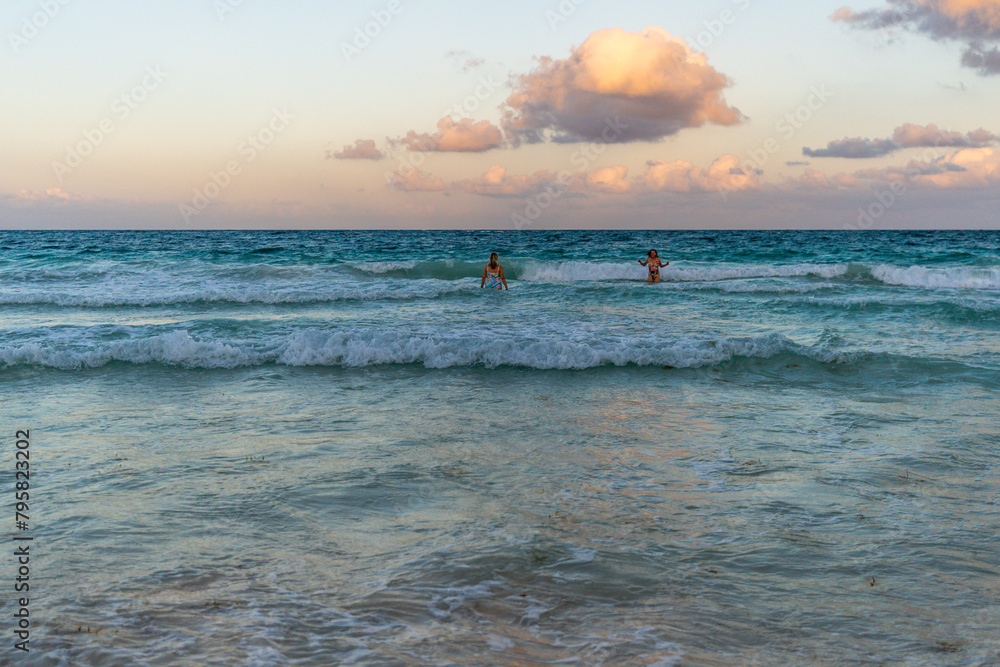 Fototapeta premium People swimming at the beach with candy floss sunset sky