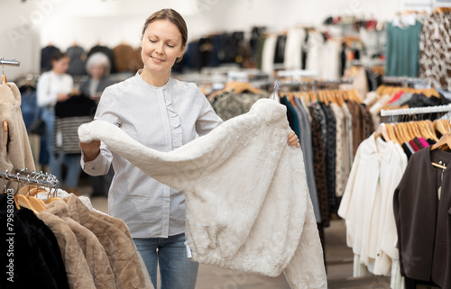 Adult woman buyer chooses fur coat in clothing store..