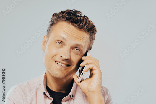 A man is talking on his cell phone while smiling. He is wearing a pink shirt. Concept of happiness and relaxation