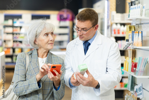 Man pharmacist talk to senior woman buyer and help to scan QR code on package, find out information about medical cosmetics. Specialist in pharmacy answer buyers question, provides consulting services