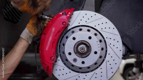 Auto mechanic replaces brake disc on car at repair shop. Hands use tools to install new pads, caliper on wheel hub. Vehicle maintenance footage for instructional, commercial, DIY project use.