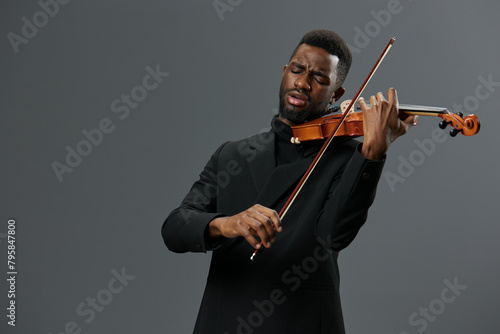 African American man in a black suit playing the violin on a gray background in a captivating musical performance portrait