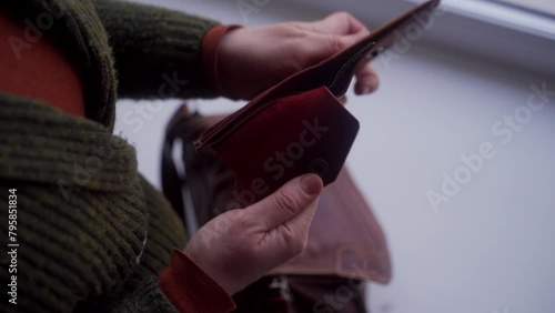 Distressed woman examines empty wallet, discovering absence of cash. Personal finance crisis, job search urgency emerge. Female checks purse, signifies poverty, need for economic assistance. photo