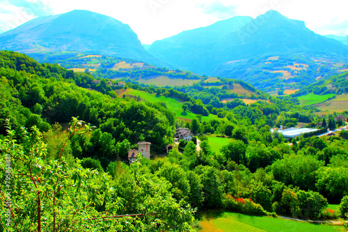 Detailed scene from Montefortino with sparkling vegetation in the foreground, buildings and roads, thickets of intense green alternating with smooth wavy meadows, and impressive Sibillini mountains