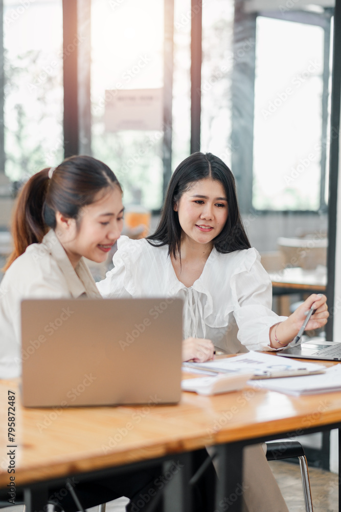 Two engaged female colleagues discuss work over a laptop in a well-lit, modern office environment. Two engaged female colleagues discuss work over a laptop in a well-lit, modern office environment.