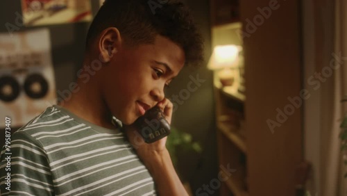 Side tilt handheld shot of Black child dialing number on vintage handset and phoning parents or friends while being alone at home with outdated interior in 90s photo