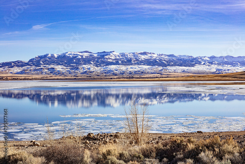 Buffalo Bill Cody Reservoir and snow-covered Carter Mountain Range during spring with ice in the water and blue cloudy sky during spring in Wyoming, USA.   photo