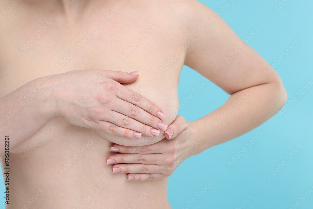 Mammology. Naked young woman doing breast self-examination on light blue background, closeup