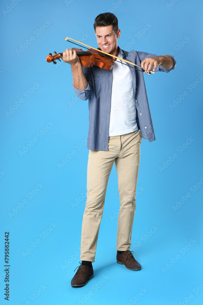 Happy man playing violin on light blue background Happy man playing violin on light blue background