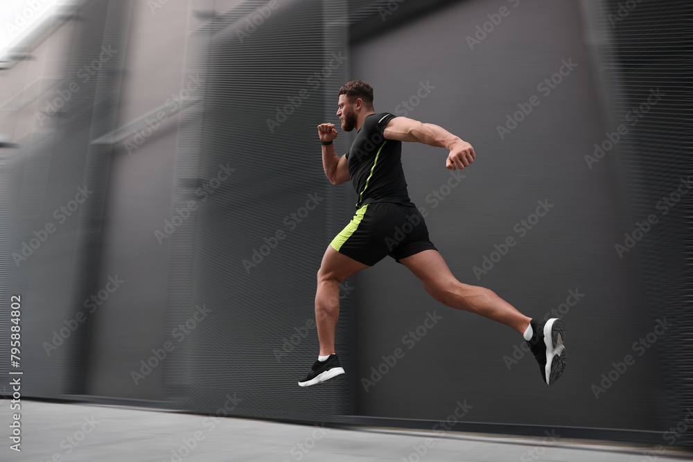 Sporty young man running on street, low angle view. Motion blur effect showing his speed