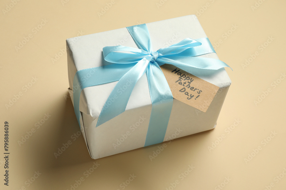 Card with phrase Happy Father's Day and gift box on beige background Card with phrase Happy Father's Day and gift box on beige background