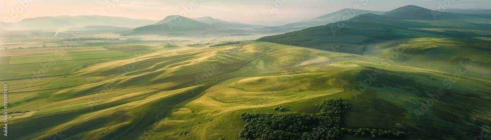 An aerial shot of a beautiful green hilly landscape with mountains in the distance. An aerial shot of a beautiful green hilly landscape with mountains in the distance.