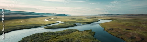 An aerial view of a meandering river in a flat green landscape with distant mountains.