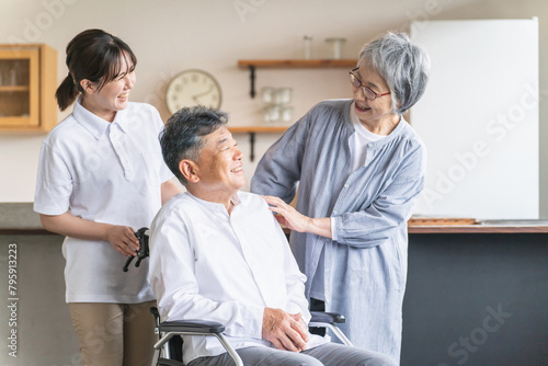 車椅子に座る高齢者男性と高齢者女性と介護士・理学療法士・介護スタッフの女性 