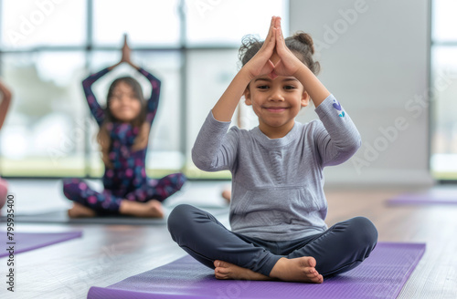 Children doing yoga in the gym, a white bright interior. Children sitting on purple yoga mats and stretching their hands up to one side.