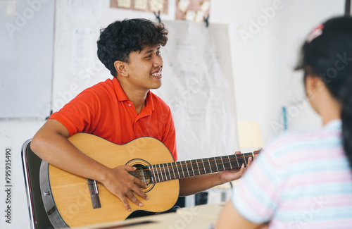 Students playing guitar during a music lesson. One boy is playing guitar and some of his peers are watching. photo