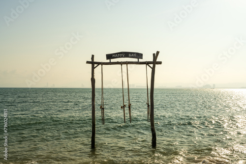 A swing with a "happy bay" board by the sea.