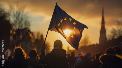 Silhouetted against the rising sun, a woman holds the European flag amidst a crowd, symbolizing unity and hope for a new day photo
