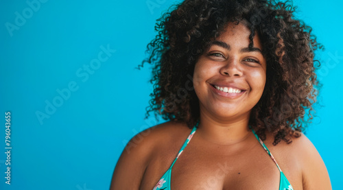 A plus size black afro-american bikini model with curly hair is smiling and wearing a bikini top © Eliya