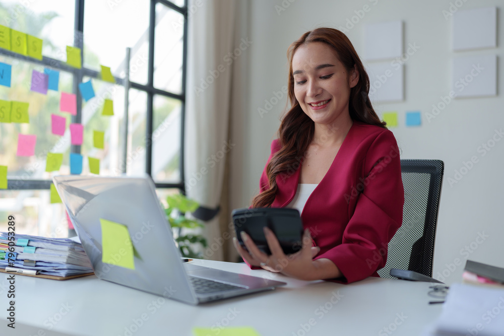 Asian businesswoman smiling at the idea of working at a calculator to calculate income. on the laptop at the office. Asian businesswoman smiling at the idea of working at a calculator to calculate income. on the laptop at the office.