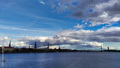 Panoramic cityscape over water, with dramatic clouds and a bridge in the distance. © Danielli.capture