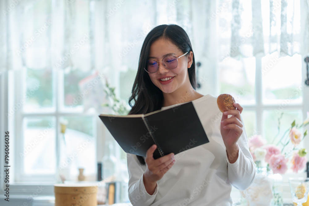 Attractive young woman wearing glasses holding a reading book and snacks stands smiling relaxedly in a bakery, shop, coffee shop in the morning. lifestyle concept working holiday. Attractive young woman wearing glasses holding a reading book and snacks stands smiling relaxedly in a bakery, shop, coffee shop in the morning. lifestyle concept working holiday.