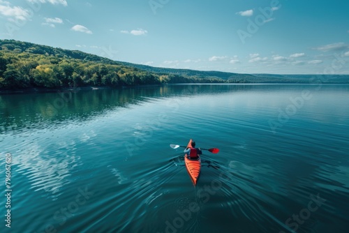 A man in a red kayak is paddling on a lake. The water is calm and the sky is clear. Concept of peace and tranquility